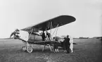 Visning av flygplan S 6, Fokker C.V. på ett flygfält. En grupp civila står vid planet. Omkring 1930.