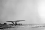 Flygplan Fokker S 6, C.V. uppställd framför CVM hangarer på Malmen, vintertid, omkring 1930. Röda och Gula förråden i bakgrunden.