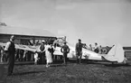 Folksamling kring civilt flygplan General Aircraft Monospar ST-4 Mk II, märkt SE-ADS på besök på Centrala verkstäderna på Malmen, 1930-tal. Vy från sidan.