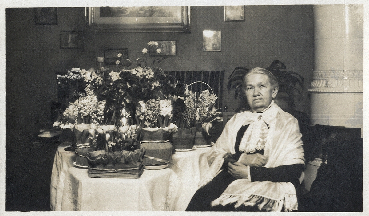 En äldre dam, fru Charlotte Pihl, på sin födelsedag (5/3 1920) med mängder av blommor.
Agghult Lillegård, Traryd.