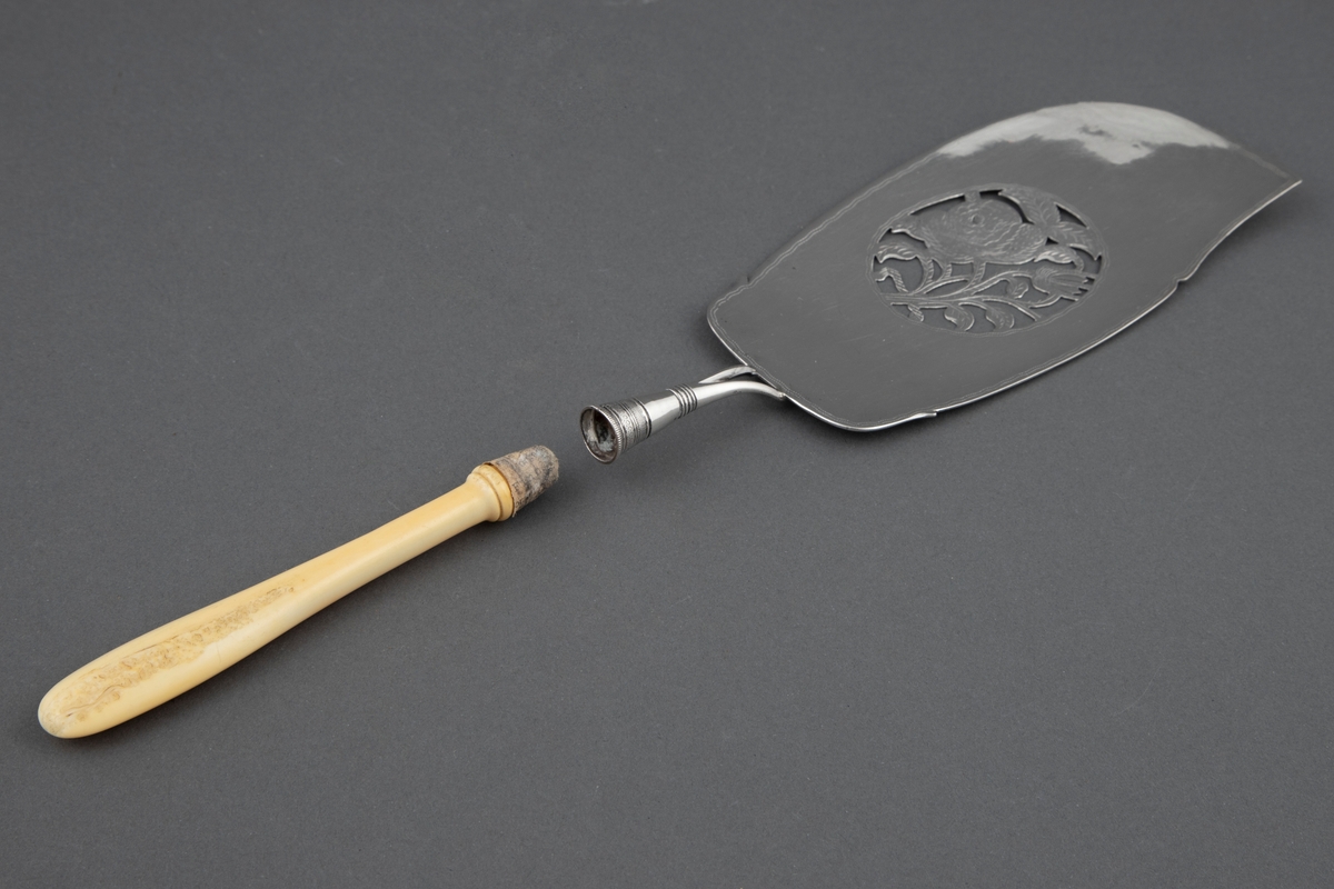 Fiskespade i sølv med gjennombrutt blad og rosemotiv. Benskaft som har løsnet i festet.