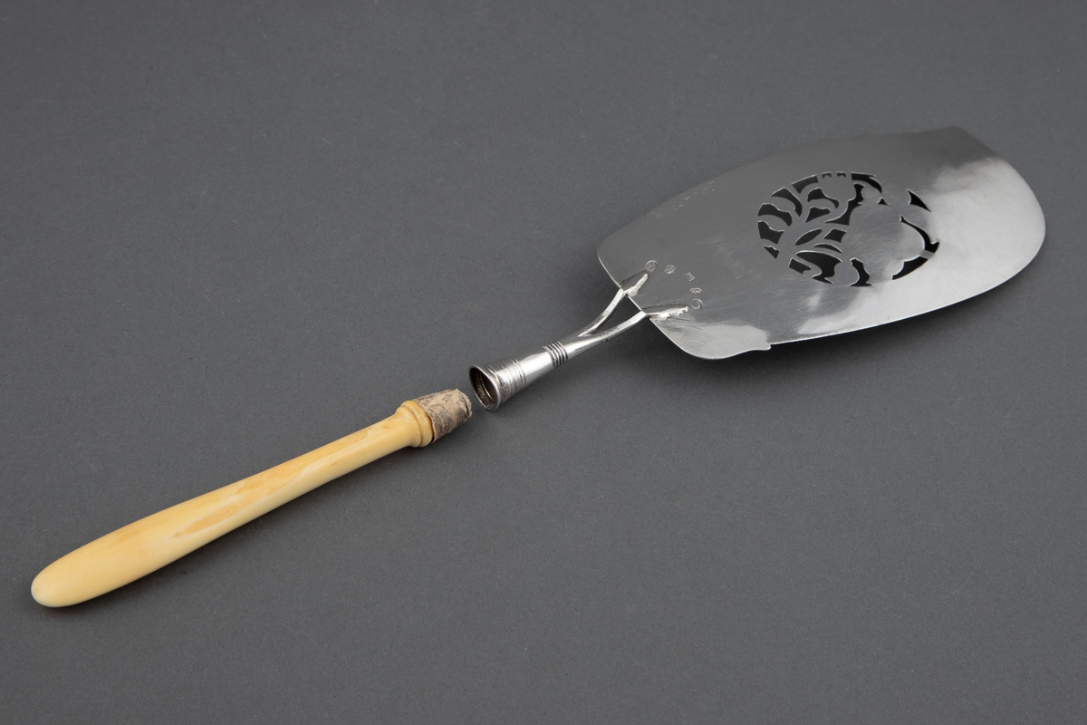 Fiskespade i sølv med gjennombrutt blad og rosemotiv. Benskaft som har løsnet i festet.
