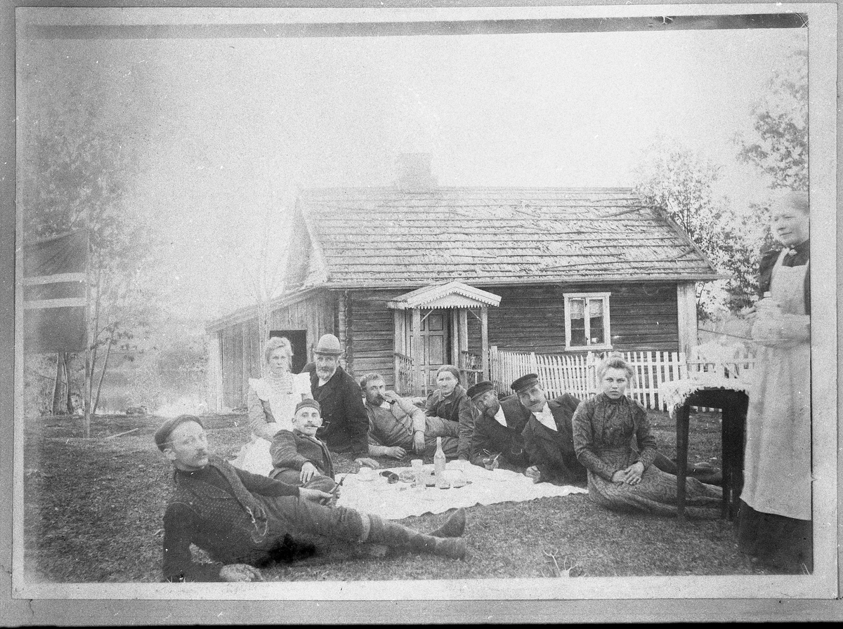 Gruppebilde fra plassen Brøttet under Sivesind, Vestre Toten, året 1902. Vi ser stua med Sivesindtjernet i bakgrunnen. Personene er (Sikker rekkefølge ukjent): Kr. Holst, Hans Chr Sivesind (antakelig mannen med hatt), Adolf Holst, Anne Holst (mor til Adolf og Gustav), Johannes Mellgarn Sivesind (trolig nr. fire fra høyre), Ole Petter Sivesind (1868-1905), Dina Sivesind (gift Felde), Johanne Bakke (trolig ytterst tul høyre; husholderske hos Hans Chr. Sivesind)