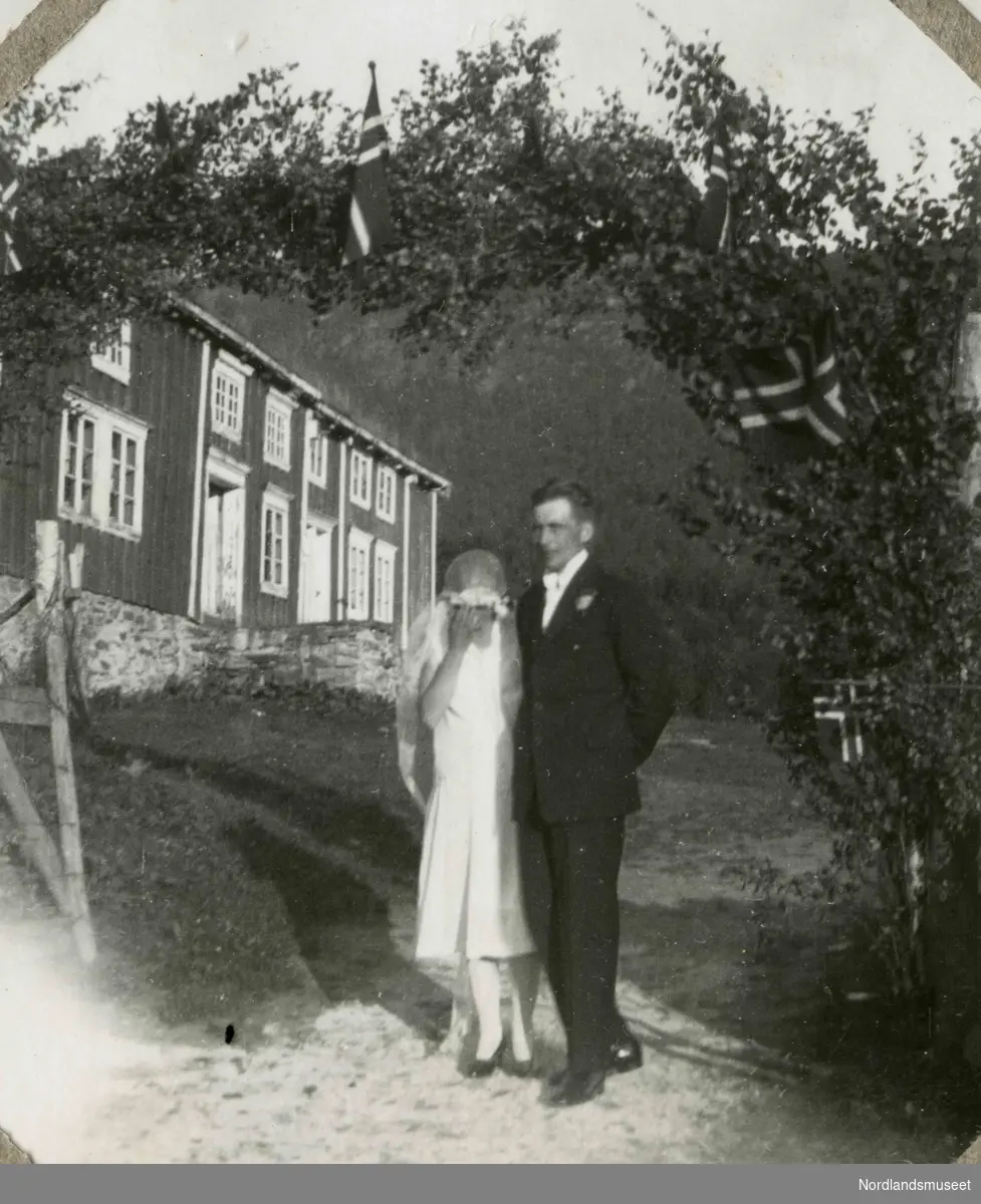 Et brudepar står fremfor et hus.