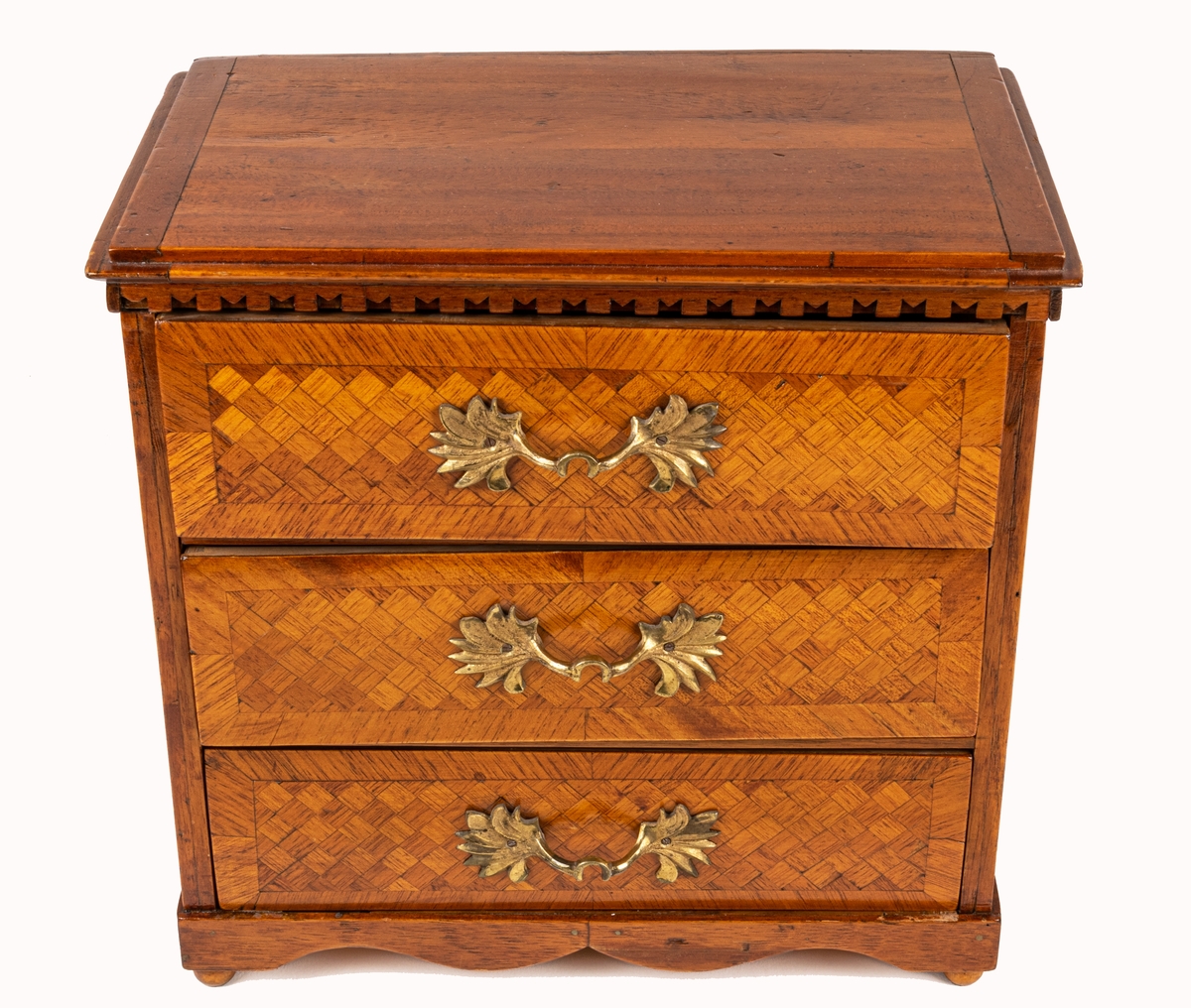 Sybyrå, barock typ, med tandning under skivans kanter. Miniatyrbyrå, med tre draglådor med fanér, delvis i rutmönster. Gjutna bronshandtag. Kulfötter. Obs. en liten smal låda upptill på byråns baksida.