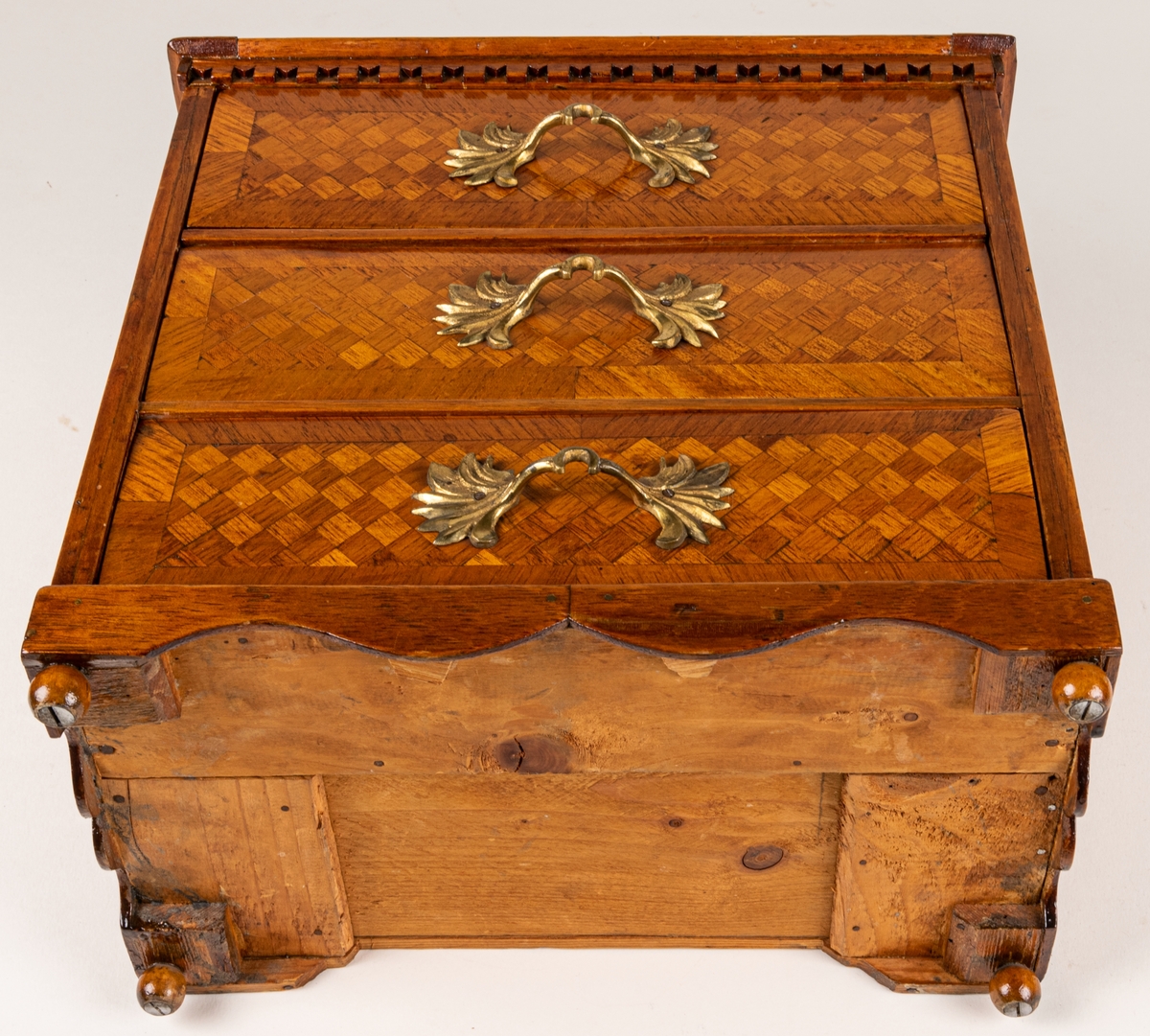 Sybyrå, barock typ, med tandning under skivans kanter. Miniatyrbyrå, med tre draglådor med fanér, delvis i rutmönster. Gjutna bronshandtag. Kulfötter. Obs. en liten smal låda upptill på byråns baksida.