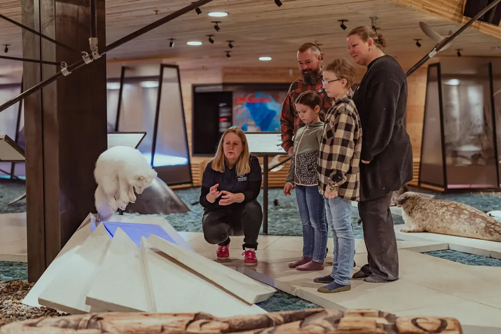 The picture shows a family with two adults and two children who together with a museum guide study a polar fox.