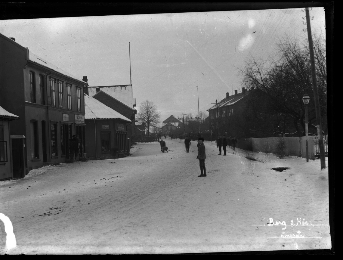 Snølagt gate med bebyggelse og mennesker.