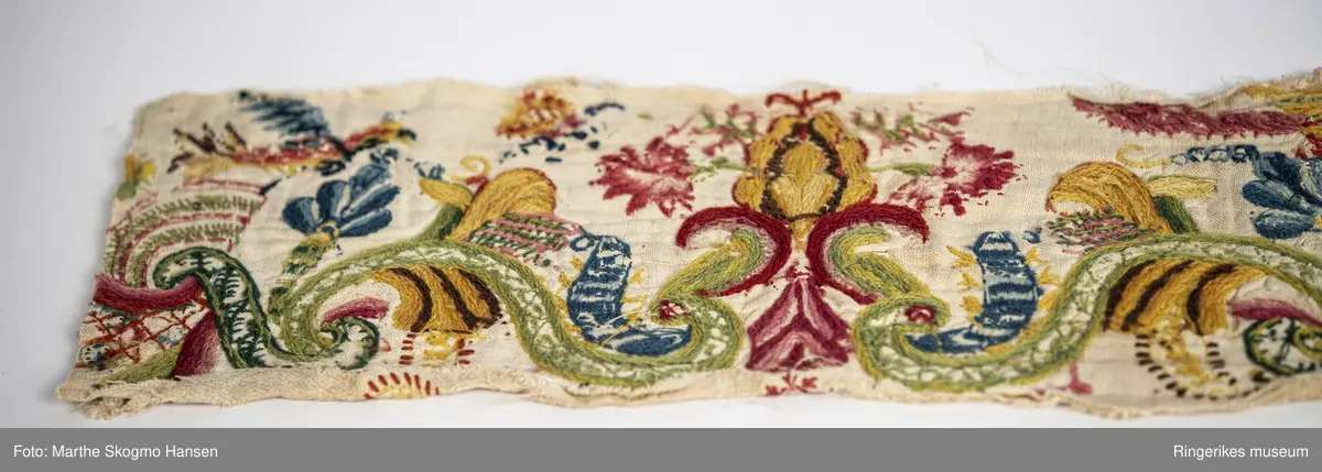 Brodert kant, enten fra en kjole eller en duk. Stoffet er vevd i diamantkypert, men på baksiden er det festet et for av lerretsbinding. Dette ble festet på før boderiet ble gjort. Mange forskjellige sting har blitt brukt i broderiet, blant annet satengsting og kjedesting (noe av dette kan muligens være tamburering). Motivene er både abstrakte og konkrete. Det er blomster (noen av dem ser ut som nelliker), insekter og fugler, men også mer abstrakte bølgemønstre som kan være inspirert av akanthusranker. På midten er det brodert et nett med bølger rundt og et opp-ned hjerte på toppen. 

Stoffet er slitt, særlig langs den nederste kanten. Noen steder er stoffet slitt helt vekk, og bare foret er igjen. Broderiene er imidlertid stort sett intakte. Fargene på forsiden er bleket, baksiden viser de opprinnelige fargene bedre.