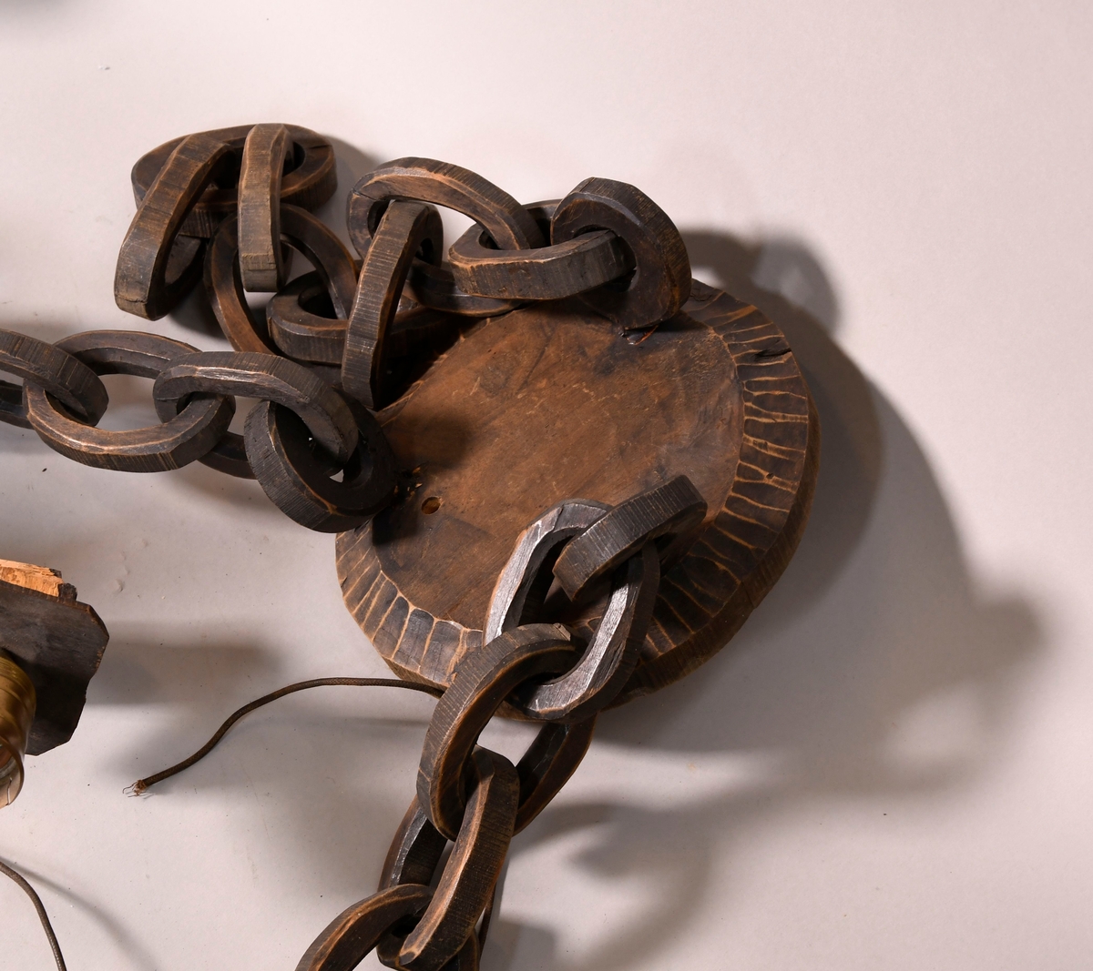 Lysekrone av tre, med seks armer. På midten er det en skåret figur av stående elg. På sidene av armene er det border med dekorative ellipser og sirkler, og en bølgeformet svai på toppen. Lysstellet henger i kjettinger av tre. Lampeskjermer av hvit tekstil er kjegleformet.