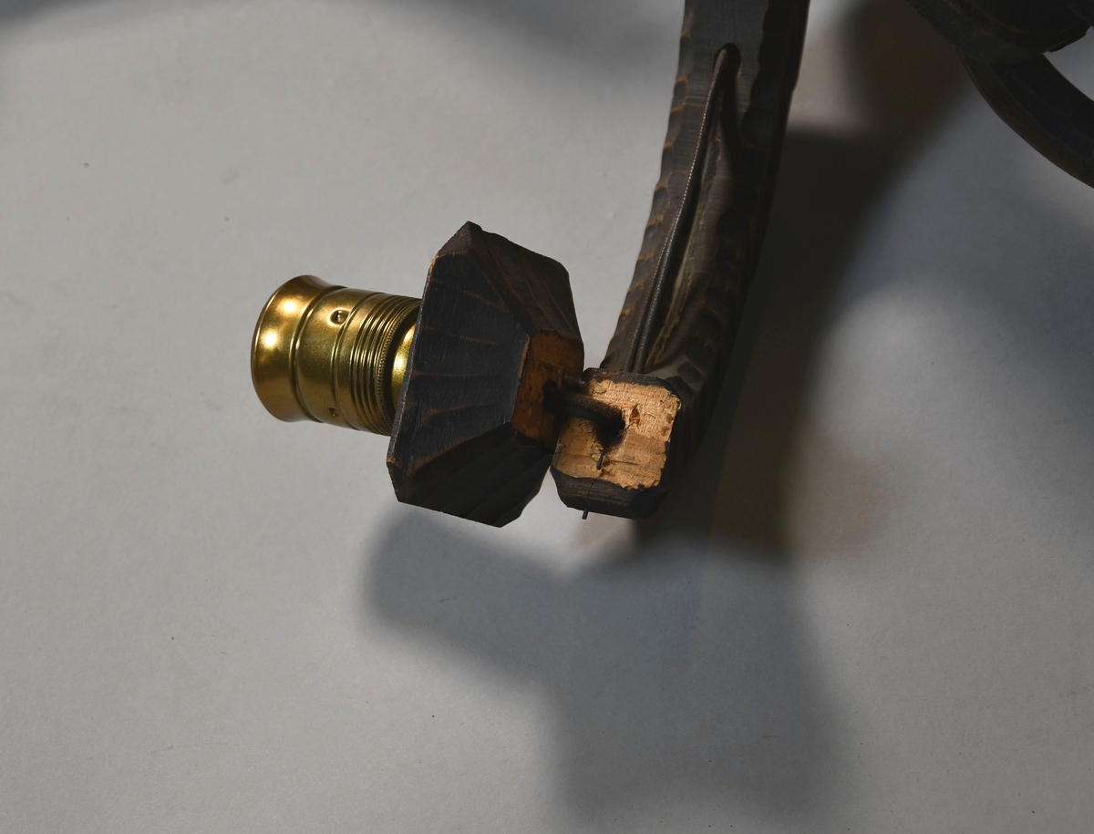 Lysekrone av tre, med seks armer. På midten er det en skåret figur av stående elg. På sidene av armene er det border med dekorative ellipser og sirkler, og en bølgeformet svai på toppen. Lysstellet henger i kjettinger av tre. Lampeskjermer av hvit tekstil er kjegleformet.