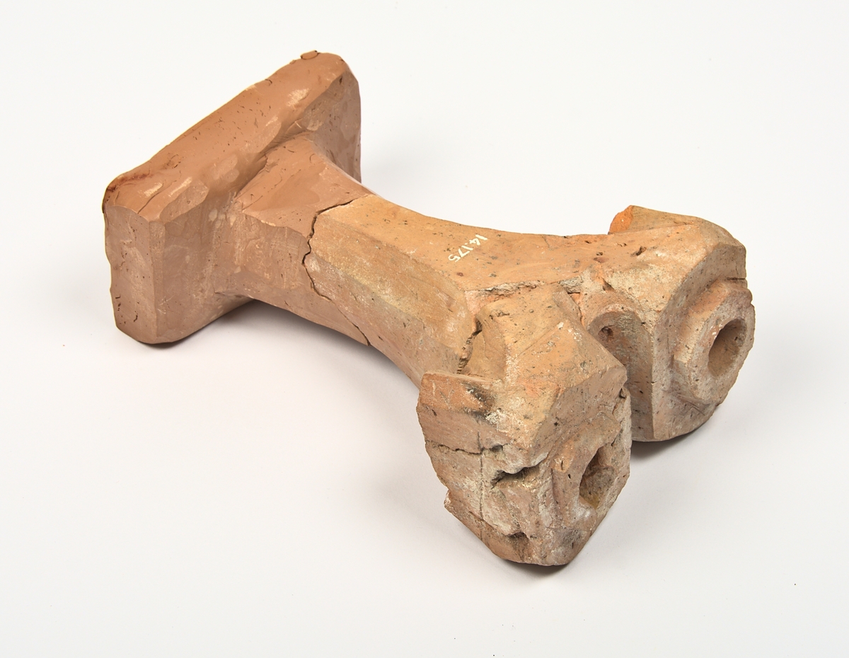 Ljusstake av oglaserat tegel. Ljusstaken har två armar med en urgröpning för ljus vardera. Skaftet är avslaget och saknas - till föremålet hör en modern rekonstruktion som visar hur skaftet kan ha sett ut; se bilder.