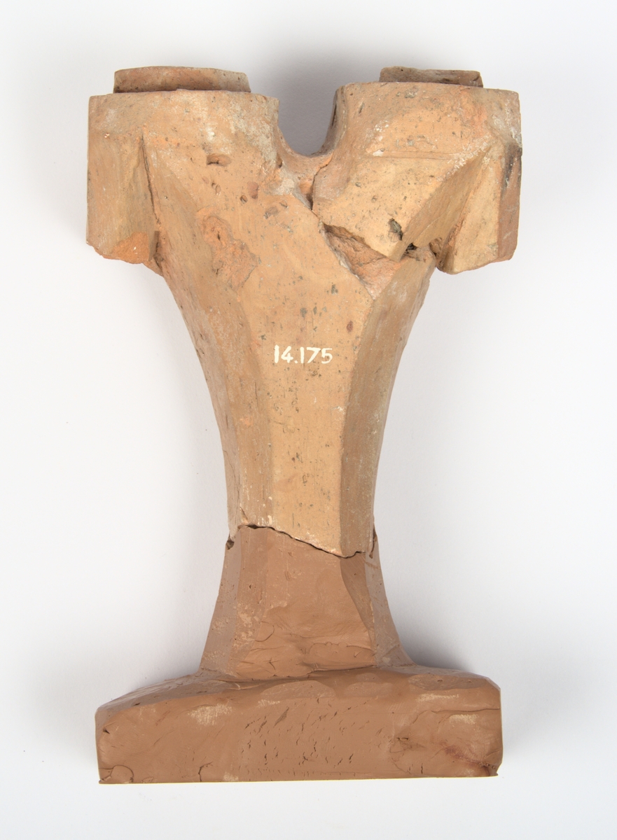 Ljusstake av oglaserat tegel. Ljusstaken har två armar med en urgröpning för ljus vardera. Skaftet är avslaget och saknas - till föremålet hör en modern rekonstruktion som visar hur skaftet kan ha sett ut; se bilder.