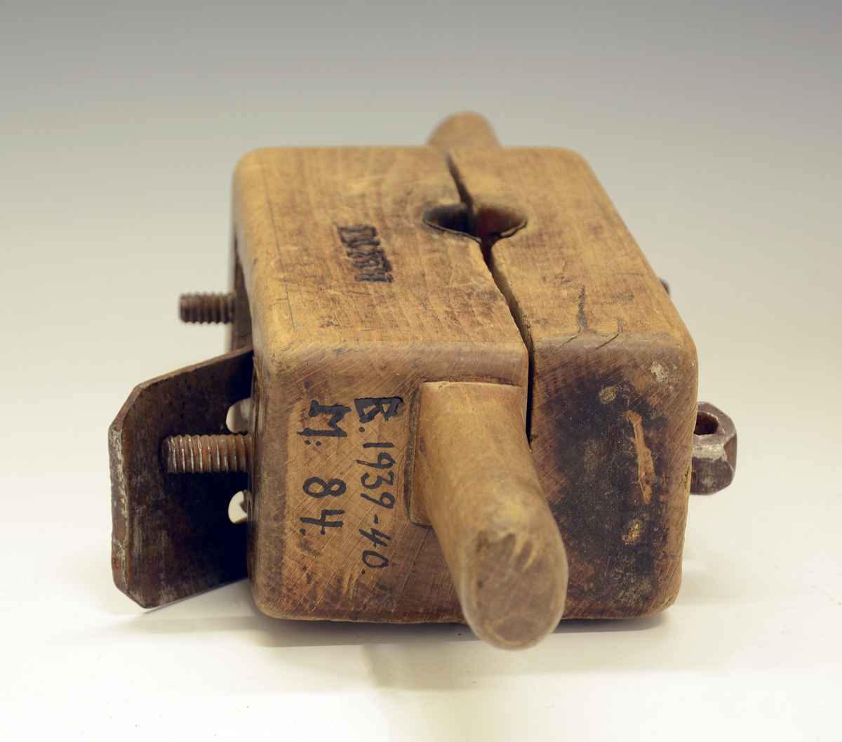 Naglelod. Redskap til å dreie skipsnagler av tre. Fra protokollen: "Nagledreie", reidskap til aa dreie skipsnaglar. Av eik (?), ihopsett av tvo rektangulære klossar (med handtak i eine enden), i principet ein hyvelstokk som i øvre tykkare halvpart hev hyveltann, og som heng ihop med undare halvpart med tvo jarnskruvar, mest som ei bokbindarklembe. Tvert igjenom baae klossane (med ei skore i kvar) gjeng eit koniskt laga hol, med koparskodde sidur, i dette holet vert trenaglen tilmaksla, i di hyvetorni gjeng inn til dette. (R. Berge)