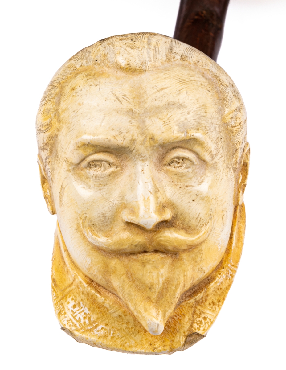 Rökpipa, snidad i sjöskum, skaft av trä med förlängning. Piphuvudet format som Gustaf II Adolfs huvud, gjort av Ida Matton, Gävle.
Texter i låg relief på sidorna:
*1594 † 1632. GUSTAF II ADOLF.
1613 Knäröd. 1617 Stolbova. 1631 Breitenfeld. 1632 Lützen.
Ida Matton Anno 1893.