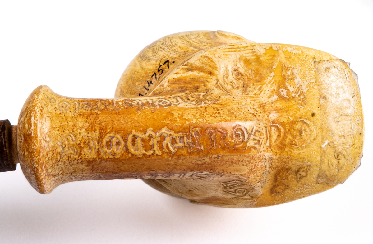 Rökpipa, snidad i sjöskum, skaft av trä med förlängning. Piphuvudet format som Gustaf II Adolfs huvud, gjort av Ida Matton, Gävle.
Texter i låg relief på sidorna:
*1594 † 1632. GUSTAF II ADOLF.
1613 Knäröd. 1617 Stolbova. 1631 Breitenfeld. 1632 Lützen.
Ida Matton Anno 1893.