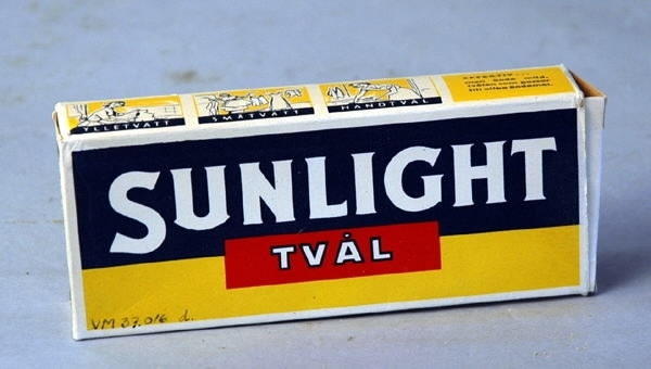 a-b) Två styck tvättvål i ett paket. Varje tvål rektangulär med stämpling på bredsidan: "Sunlight tvål", gulbrun färg. c) Tvålarna omslagna av ett vitt vaxat papper. d) Ytterkartong med öppning i kortändarna. Text som på tvålarna samt bilder av tvättande kvinna. Tillverkad av AA Sunlight, Nyköping. Tryckfärger på kartongen i blått, vitt, gult och rött.