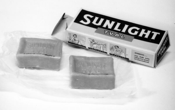 a-b) Två styck tvättvål i ett paket. Varje tvål rektangulär med stämpling på bredsidan: "Sunlight tvål", gulbrun färg. c) Tvålarna omslagna av ett vitt vaxat papper. d) Ytterkartong med öppning i kortändarna. Text som på tvålarna samt bilder av tvättande kvinna. Tillverkad av AA Sunlight, Nyköping. Tryckfärger på kartongen i blått, vitt, gult och rött.
