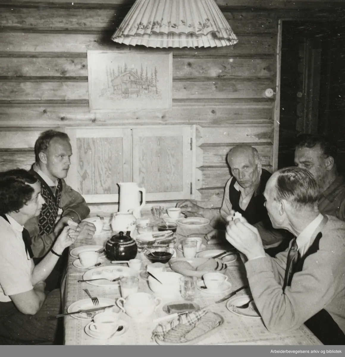 Martin Tranmæl inntil veggen på høyre side i Martinhytta, Kroken, Maridalen Oslo. 1957. Bildetekst: Vår i Maridalen, besøk av Olaf Nordskog. (Han med ryggen til )