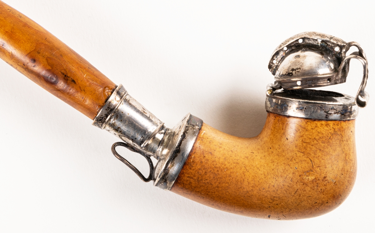 Långpipa, av sjöskum, med träskaft och benmunstycke. Silverbeslag med stämplar: "G5", "AA", samt tre kronor. År 1861.