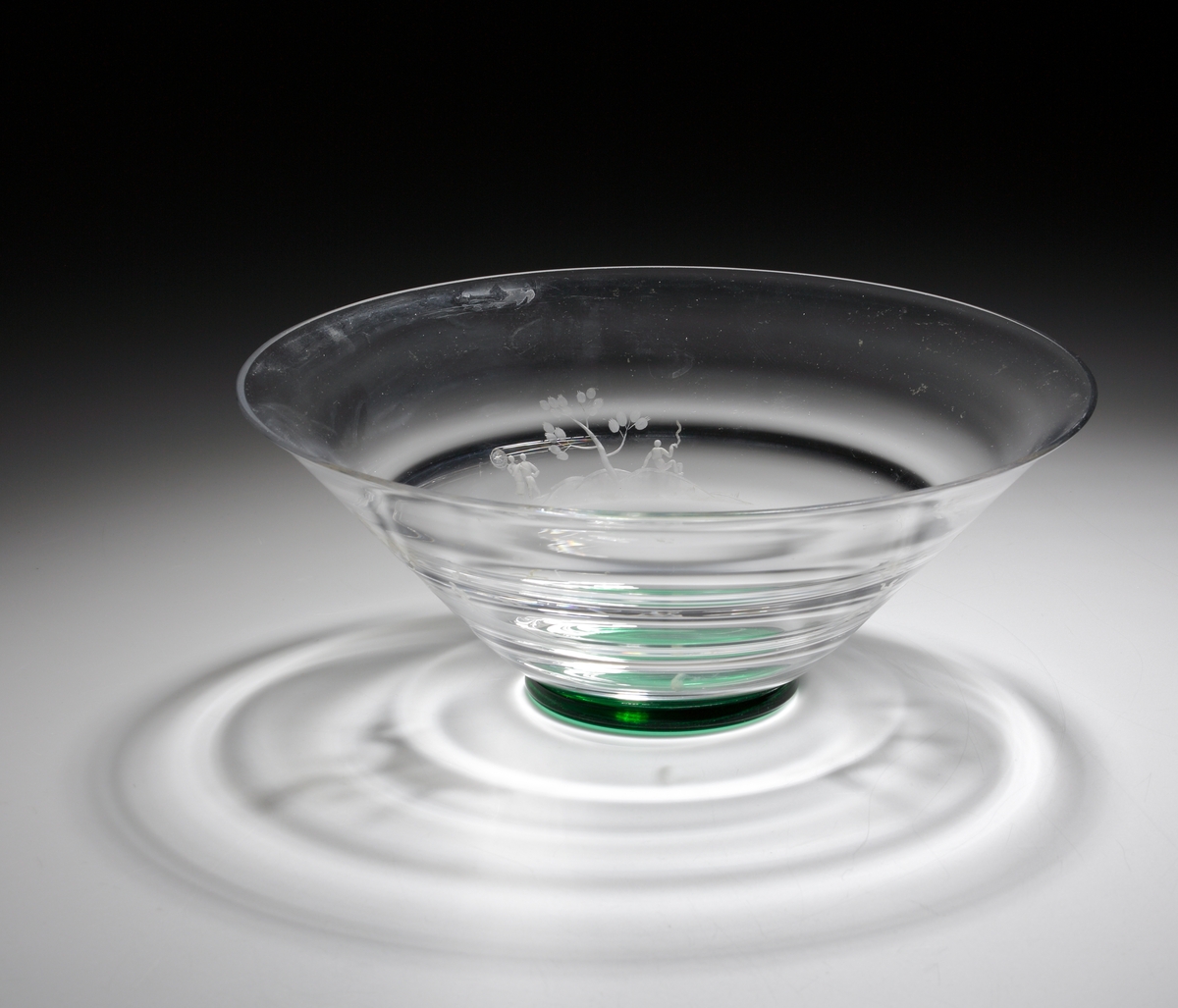 Formgiven av Nils Landberg. Konande skål med liggande optik och grön klack. Skålen graverad med tre olika ömotiv med människofigurer som fiskar, badar och har utflykt.
Ref: Gustav Abels del 2: ”Landberg 1932. Ganska goda försäljningar.”