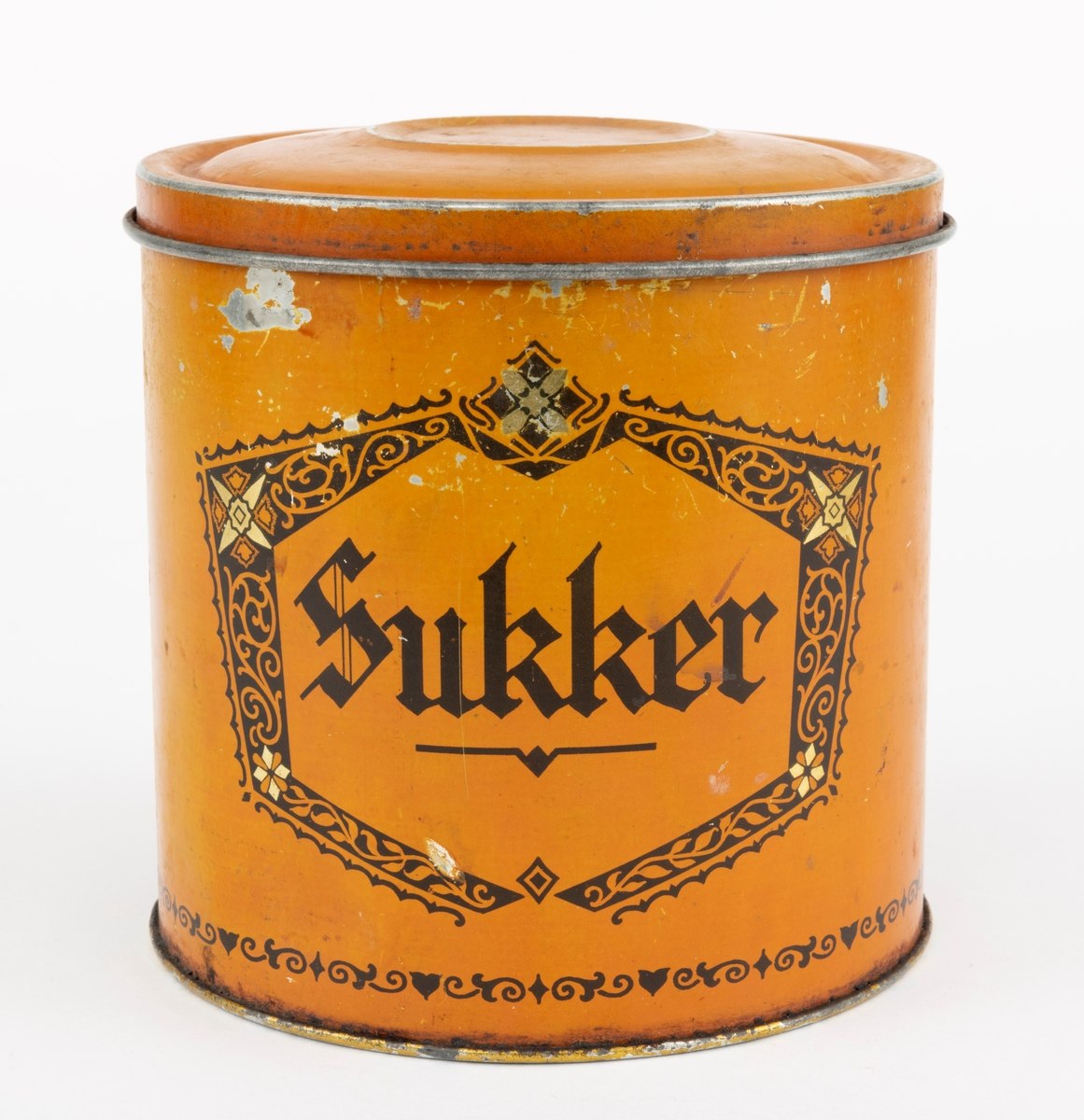 Boks med lokk, lagd av jernblikk. Boksen er sylindrisk, med drøyt 15,0 centimeters diameter (midtmål) og høyden er 14,9 centimeter. Botnplata er falset til sideveggene slik at diameteren akkurat der er 15,4 centimeter. Ytterflatene på boksen er lakkert med  en lys sennepsgul grunnfarge. På dette underlaget er ordet «Sukker» - omgitt av ei sekskantet ramme med rankeornamenter - påtrykt med svart farge. Også langs den nedre delen av sideflata er det påtrykt en svartfarget bord. Standflata og overkanten, som skal omsluttes av lokkets ytterkant, er lakkert med en farge som gir en illusjon av gull. «Baksida» av ytterflata har et ovalt emblem med strektening av et jentebarn og en liten hund som biter henne i skjørtekanten, med underteksten «INDREGISTRERET VARE-MERKE». Under denne finner vi teksten «Lorentz Erbe & Søn  ETABL. 1875 TRONDHJEM  KJEKS-KARAMEL-PEPPERMYNTE-KNEKKEBRØDFABRIKKER».

Lokket er presset i en rund form og med en diameter som skal omslutte boksens overkant såpass tett at det oppstår vakuum som virker konserverende på innholdet. Diameteren ved lokkanten, som er utoverfalset, er 15,6 centimeter. Lokket er noe oppoverbuket, men med en antydning til ei lita skål i sentrum. Ytterflatene på denne komponentene er lakkert med samme lyst sennepsgule farge som boksens utvendige sideflate, men lokket har ingen påstemplet fargedekor.

Boksen rommer 2,5 liter.