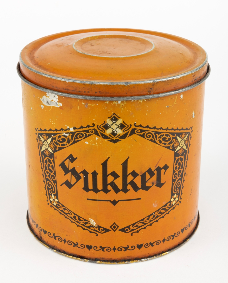 Boks med lokk, lagd av jernblikk. Boksen er sylindrisk, med drøyt 15,0 centimeters diameter (midtmål) og høyden er 14,9 centimeter. Botnplata er falset til sideveggene slik at diameteren akkurat der er 15,4 centimeter. Ytterflatene på boksen er lakkert med  en lys sennepsgul grunnfarge. På dette underlaget er ordet «Sukker» - omgitt av ei sekskantet ramme med rankeornamenter - påtrykt med svart farge. Også langs den nedre delen av sideflata er det påtrykt en svartfarget bord. Standflata og overkanten, som skal omsluttes av lokkets ytterkant, er lakkert med en farge som gir en illusjon av gull. «Baksida» av ytterflata har et ovalt emblem med strektening av et jentebarn og en liten hund som biter henne i skjørtekanten, med underteksten «INDREGISTRERET VARE-MERKE». Under denne finner vi teksten «Lorentz Erbe & Søn  ETABL. 1875 TRONDHJEM  KJEKS-KARAMEL-PEPPERMYNTE-KNEKKEBRØDFABRIKKER».

Lokket er presset i en rund form og med en diameter som skal omslutte boksens overkant såpass tett at det oppstår vakuum som virker konserverende på innholdet. Diameteren ved lokkanten, som er utoverfalset, er 15,6 centimeter. Lokket er noe oppoverbuket, men med en antydning til ei lita skål i sentrum. Ytterflatene på denne komponentene er lakkert med samme lyst sennepsgule farge som boksens utvendige sideflate, men lokket har ingen påstemplet fargedekor.

Boksen rommer 2,5 liter.