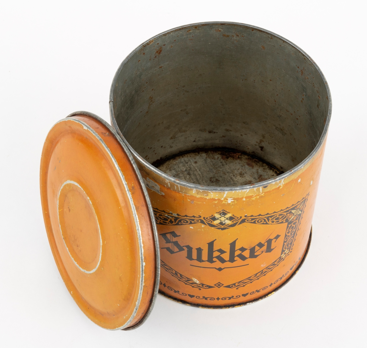 Boks med lokk, lagd av jernblikk. Boksen er sylindrisk, med drøyt 15,0 centimeters diameter (midtmål) og høyden er 14,9 centimeter. Botnplata er falset til sideveggene slik at diameteren akkurat der er 15,4 centimeter. Ytterflatene på boksen er lakkert med  en lys sennepsgul grunnfarge. På dette underlaget er ordet «Sukker» - omgitt av ei sekskantet ramme med rankeornamenter - påtrykt med svart farge. Også langs den nedre delen av sideflata er det påtrykt en svartfarget bord. Standflata og overkanten, som skal omsluttes av lokkets ytterkant, er lakkert med en farge som gir en illusjon av gull. «Baksida» av ytterflata har et ovalt emblem med strektening av et jentebarn og en liten hund som biter henne i skjørtekanten, med underteksten «INDREGISTRERET VARE-MERKE». Under denne finner vi teksten «Lorentz Erbe & Søn  ETABL. 1875 TRONDHJEM  KJEKS-KARAMEL-PEPPERMYNTE-KNEKKEBRØDFABRIKKER».

Lokket er presset i en rund form og med en diameter som skal omslutte boksens overkant såpass tett at det oppstår vakuum som virker konserverende på innholdet. Diameteren ved lokkanten, som er utoverfalset, er 15,6 centimeter. Lokket er noe oppoverbuket, men med en antydning til ei lita skål i sentrum. Ytterflatene på denne komponentene er lakkert med samme lyst sennepsgule farge som boksens utvendige sideflate, men lokket har ingen påstemplet fargedekor.

Boksen rommer 2,5 liter.