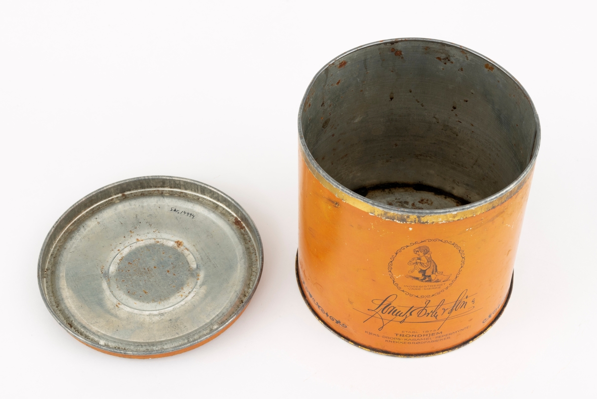 Boks med lokk, lagd av jernblikk. Boksen er sylindrisk, med drøyt 15,0 centimeters diameter (midtmål) og høyden er 14,9 centimeter. Botnplata er falset til sideveggene slik at diameteren akkurat der er 15,4 centimeter. Ytterflatene på boksen er lakkert med  en lys sennepsgul grunnfarge. På dette underlaget er ordet «Sukker» - omgitt av ei sekskantet ramme med rankeornamenter - påtrykt med svart farge. Også langs den nedre delen av sideflata er det påtrykt en svartfarget bord. Standflata og overkanten, som skal omsluttes av lokkets ytterkant, er lakkert med en farge som gir en illusjon av gull. «Baksida» av ytterflata har et ovalt emblem med strektening av et jentebarn og en liten hund som biter henne i skjørtekanten, med underteksten «INDREGISTRERET VARE-MERKE». Under denne finner vi teksten «Lorentz Erbe & Søn  ETABL. 1875 TRONDHJEM  KJEKS-KARAMEL-PEPPERMYNTE-KNEKKEBRØDFABRIKKER».

Lokket er presset i en rund form og med en diameter som skal omslutte boksens overkant såpass tett at det oppstår vakuum som virker konserverende på innholdet. Diameteren ved lokkanten, som er utoverfalset, er 15,6 centimeter. Lokket er noe oppoverbuket, men med en antydning til ei lita skål i sentrum. Ytterflatene på denne komponentene er lakkert med samme lyst sennepsgule farge som boksens utvendige sideflate, men lokket har ingen påstemplet fargedekor.

Boksen rommer 2,5 liter.