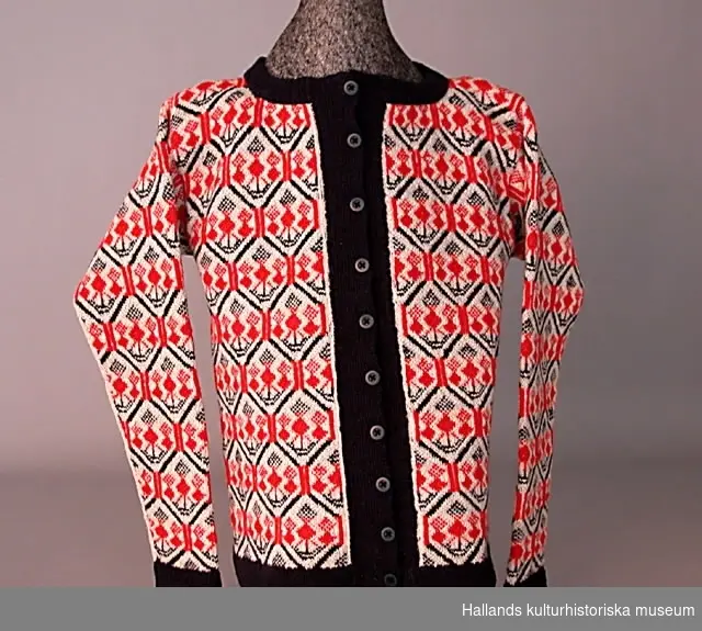 Tröja stickad i Bjärbomönster. Lång ärm. Slätstickning. Vit bottenfärg, mönsterfärger rött och blått. Muddar, nederkant, slåar fram och runt halsen resårstickning i blått. Stickad på rundsticka, uppklippt fram. Knäpps med tio knappar.