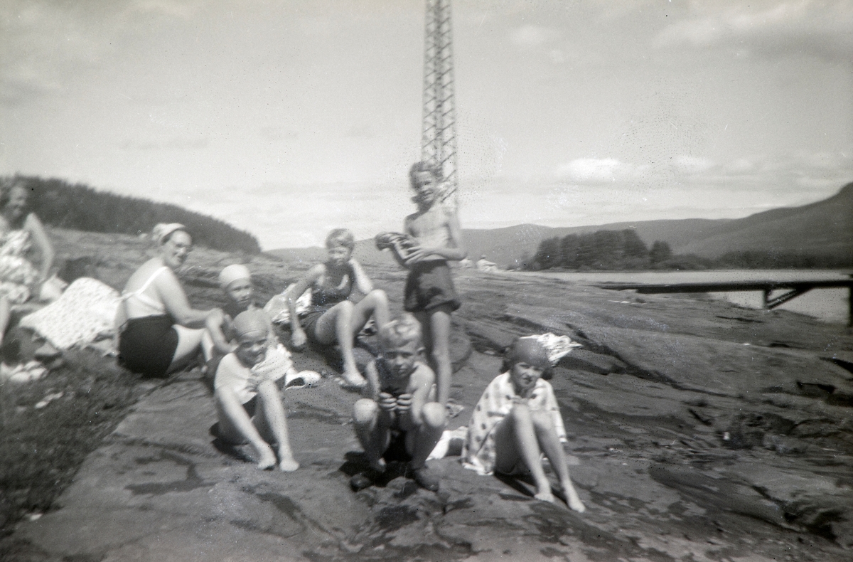 Gruppe badegjester ved Mjøsa. Fra venstre: Andrea Margrethe Glærum, født Gjestvang (1914-1993). Valborg Taroline Alhaug, født Gjestvang (1904-1992). Sedsel Gudrun Alhaug (1946-2020). Eli Kerstin Kvakkestad, født Alhaug (1944). Stående Ragnhild Glærum (1945).  Eli Vesaas, født Glærum (1947). Christen Alhaug (1947). Anne Gjestvang Bryhni,  født Gjestvang (1946).