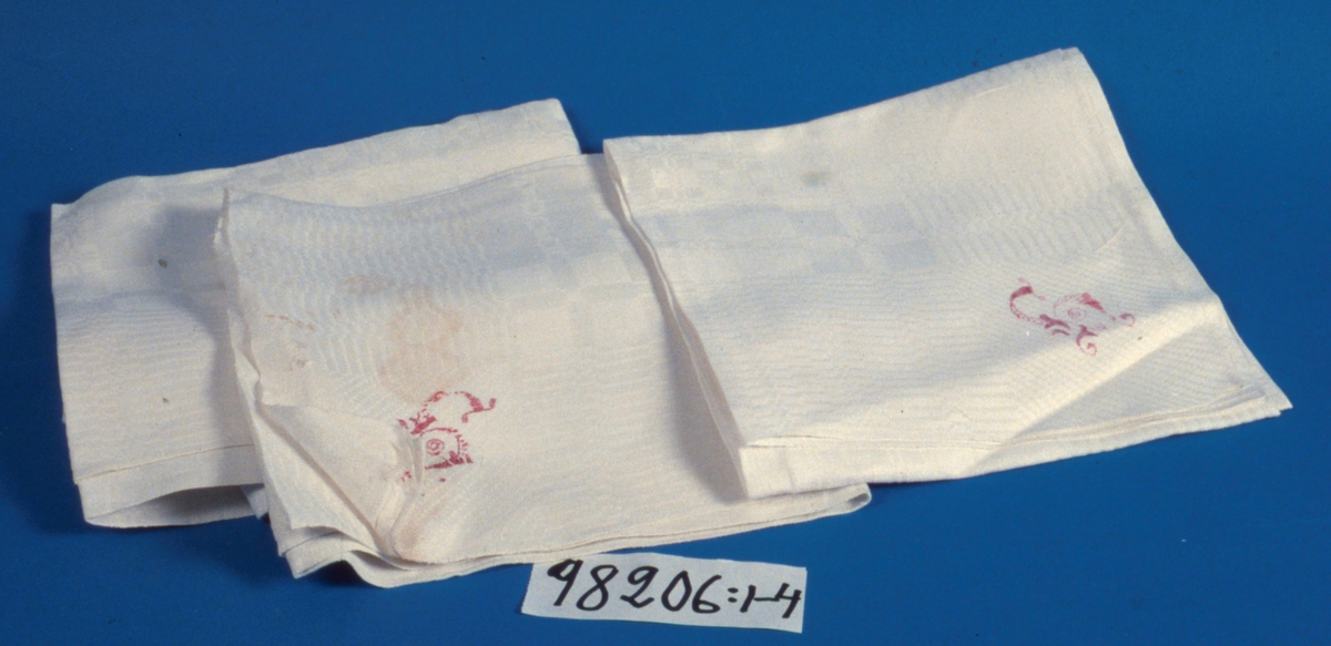 Servetter, 4 st, av vitt hellinne i rutigt drällmönster.
I ena hörnet monogram i rött, troligen "L".
Handfållade.