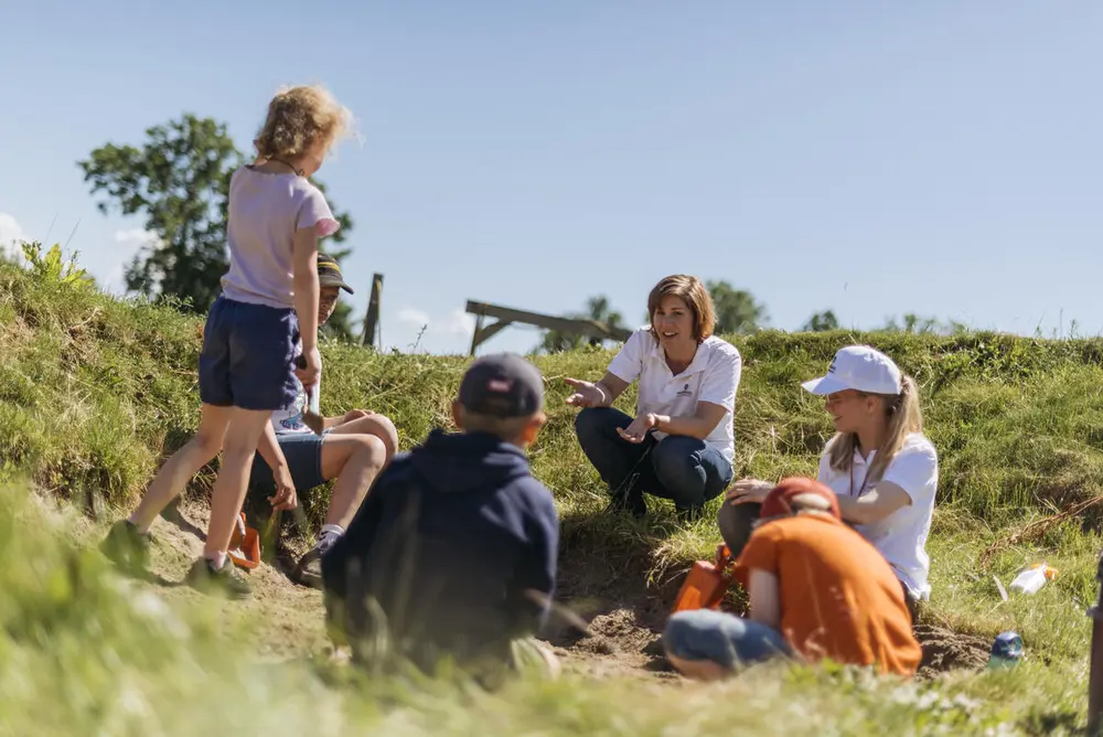 Barn leker ute i gresset, noen sitter og noen står. Det er sol