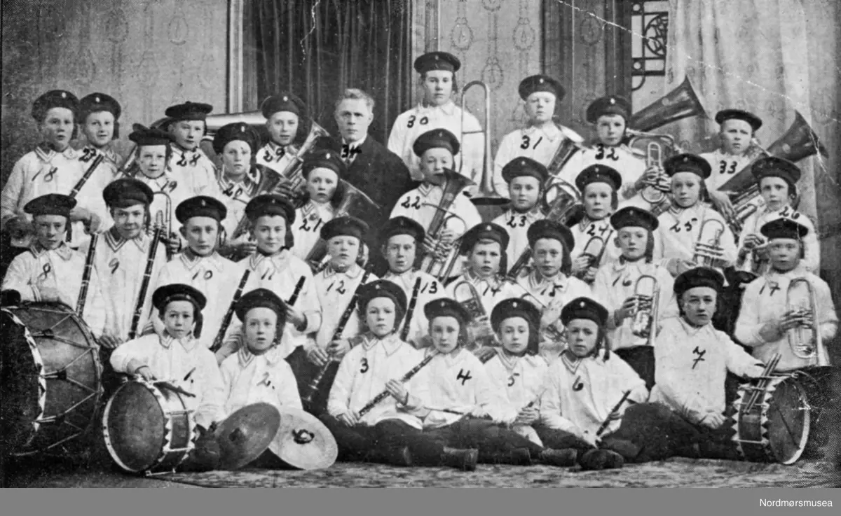 Kristiansunds gutemusikkorps 1918. På bildet ser vi: 1. Herlof Harstad, 2. Johan Pettersen, 3. Olaf Olsen, 4. Harald Lie, 5. Karl Erlandsen, 6. Sigurd Skjærseth, 7. Hans Harstad, 8. Ansgar Torkildsen, 9. Alf Bardal, 10. Oskar Olsen, 11. Kåre Dyvik, 12. Henry Jakobsen, 13. Hans Larsen, 14. Leonhard Løberg, 15. Odd Egge, 16. Jens Nilsen, 17. Olle Flakke, 18. Torger Kulø, 19. Sverre Tørlen, 20. Dagfin Schau, 21. Olaf Meek, 22. Knut Harstad, 23. Karsten Sunde, 24. Johan Røe, 25. Håkon Torkildsen, 26. Olaf Løberg, 27. Oluf Olsen, 28. Harald Haln, 29. Erling Halseth, 30. Magnar Glenes(?), 31. Olaf Halten, 32. Torleif Halseth, 33. Birger Hodne, 34. Ole Egge, dirigent, millitærmusiker og fotograf i Kristiansund. Fotografier fra protokollen til Kristiansunds Guttemusikkorps i perioden 1917-1927. Protokollførere var brødrene Hans og Herlof Harstad. Står trolig også bak de fleste fotografiene med unntak av de store gruppebildene hvor dirigent/fotograf Ole Egge fotograferte i sitt atelier. Protokollen er i museets privatarkiv under nr. 684. Giver av protokollen er Knut Harstad. Fra Nordmørsmusea sin fotosamling.
