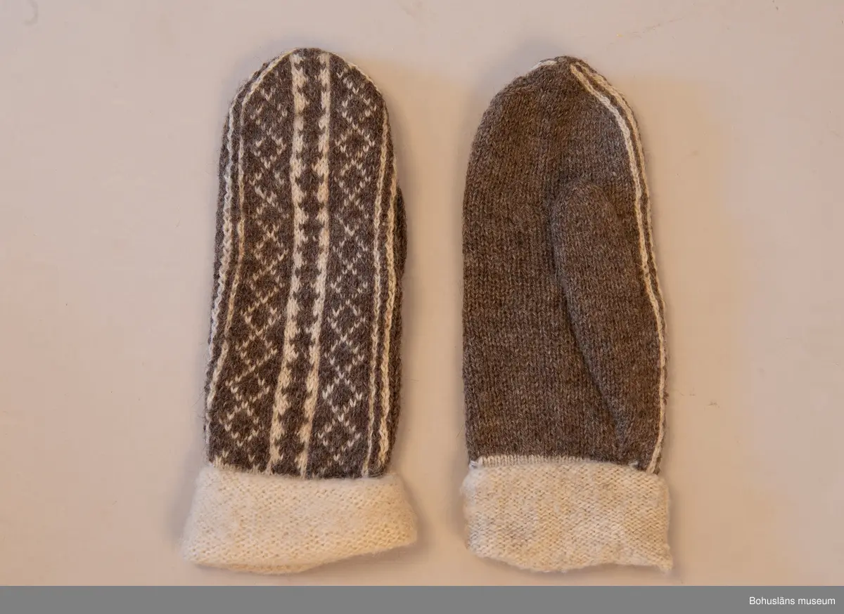 Stickade tumvantar i slätstickning med slätstickad mudd, med avigsidan utåt och mönstrat parti på ovansidan. Partiet är mönsterstickat i brunt och vitt mot en brun botten. Muddarna är stickade i naturfärgad ull som sedan blivit uppruggade med borste. Mönstret "Vävnaden" är komponerat av Emma Jacobsson. Litet slitna men välbevarade.