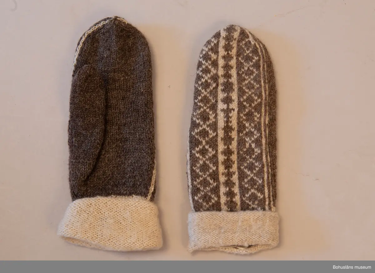 Stickade tumvantar i slätstickning med slätstickad mudd, med avigsidan utåt och mönstrat parti på ovansidan. Partiet är mönsterstickat i brunt och vitt mot en brun botten. Muddarna är stickade i naturfärgad ull som sedan blivit uppruggade med borste. Mönstret "Vävnaden" är komponerat av Emma Jacobsson. Litet slitna men välbevarade.