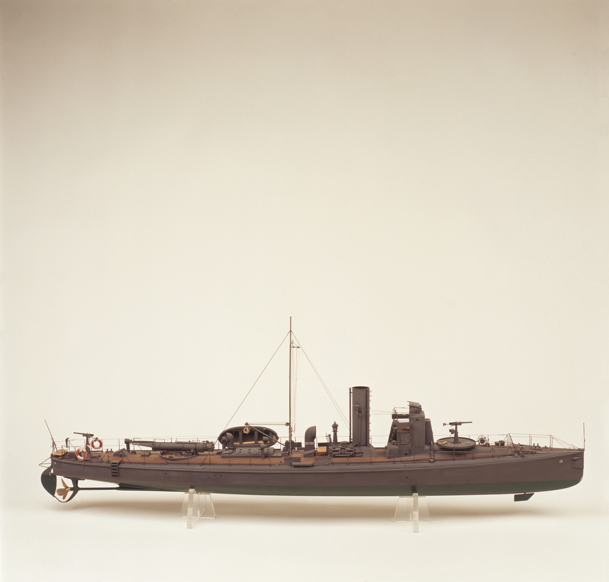 Fartygsmodell. Lamellbyggd, fullständig däcksinredning, för- och akterroder, metallpropeller. Riggad mast med vimpel, flaggspel med flagga, gösstake med gös. Gråmålad, grön botten, korkfärgat däck. 1 kanon. I stävarna märkt  '12” med vita siffror. 1 jolle med inredning, roder och 2 st åror. Stativ: 2 mässingspelare.