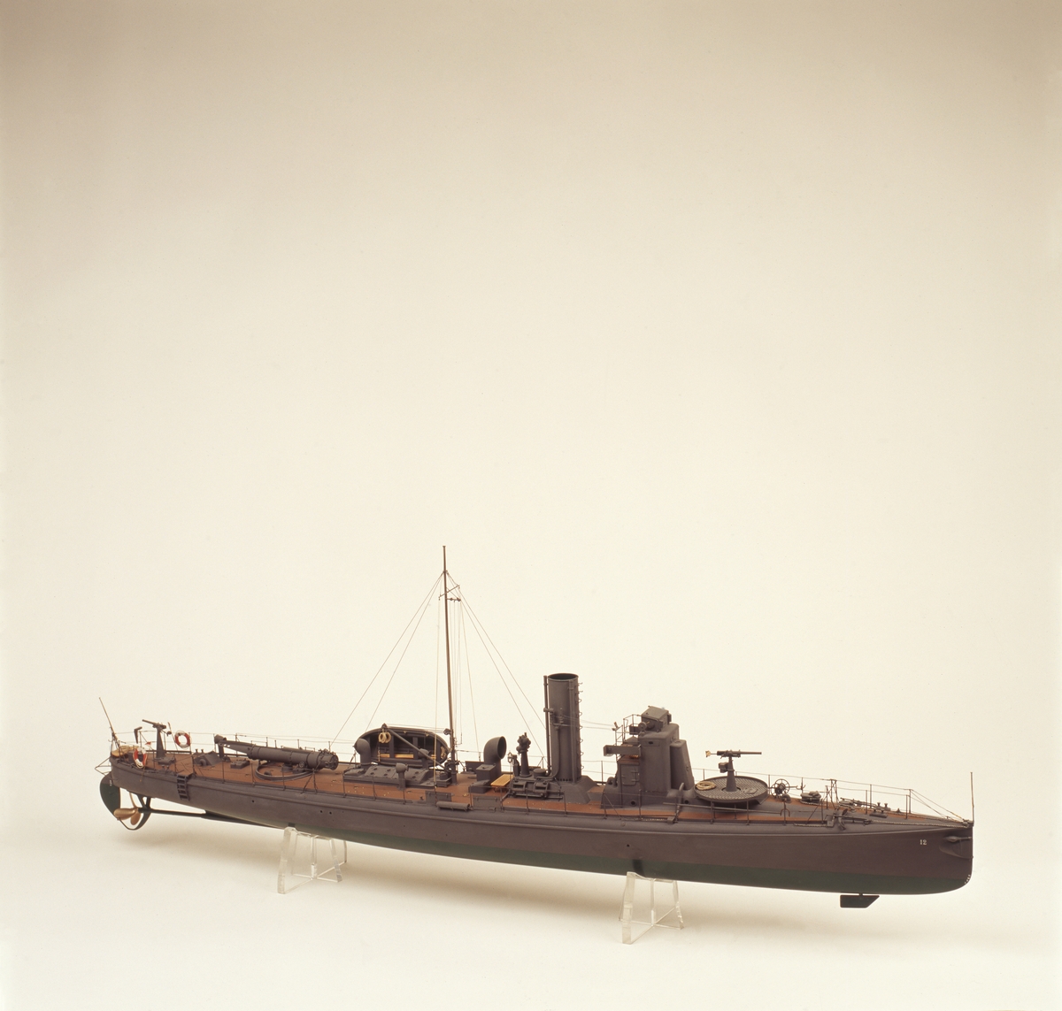 Fartygsmodell. Lamellbyggd, fullständig däcksinredning, för- och akterroder, metallpropeller. Riggad mast med vimpel, flaggspel med flagga, gösstake med gös. Gråmålad, grön botten, korkfärgat däck. 1 kanon. I stävarna märkt  '12” med vita siffror. 1 jolle med inredning, roder och 2 st åror. Stativ: 2 mässingspelare.