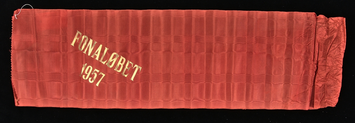 Rött konstsidenband med målad guldtext: "FONALÖBET 1957".
