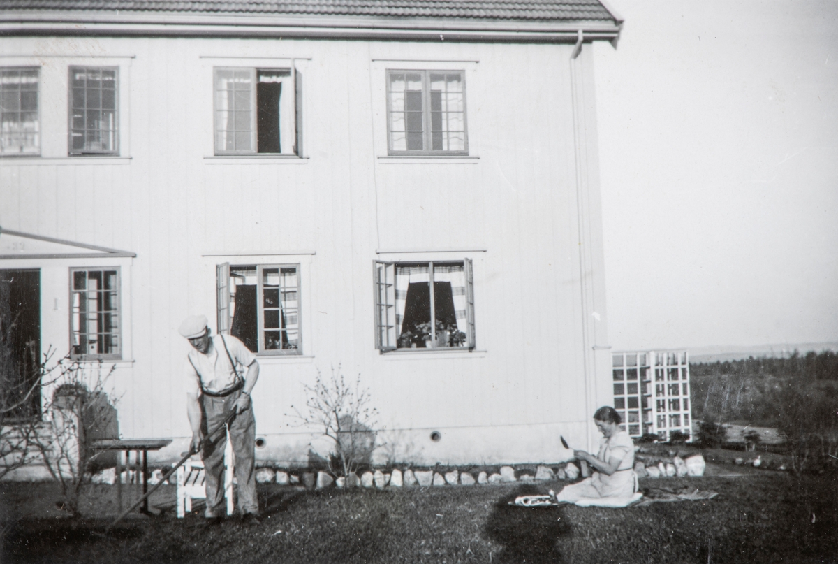 Hagearbeid i hagen på Grylling, Ola Storbæk med rive, Oddrun Storbæk sitter på bakken. Nyanlagte hage, plantebed med steinkant, hagemøbler. Slutten av 1930-tallet.
