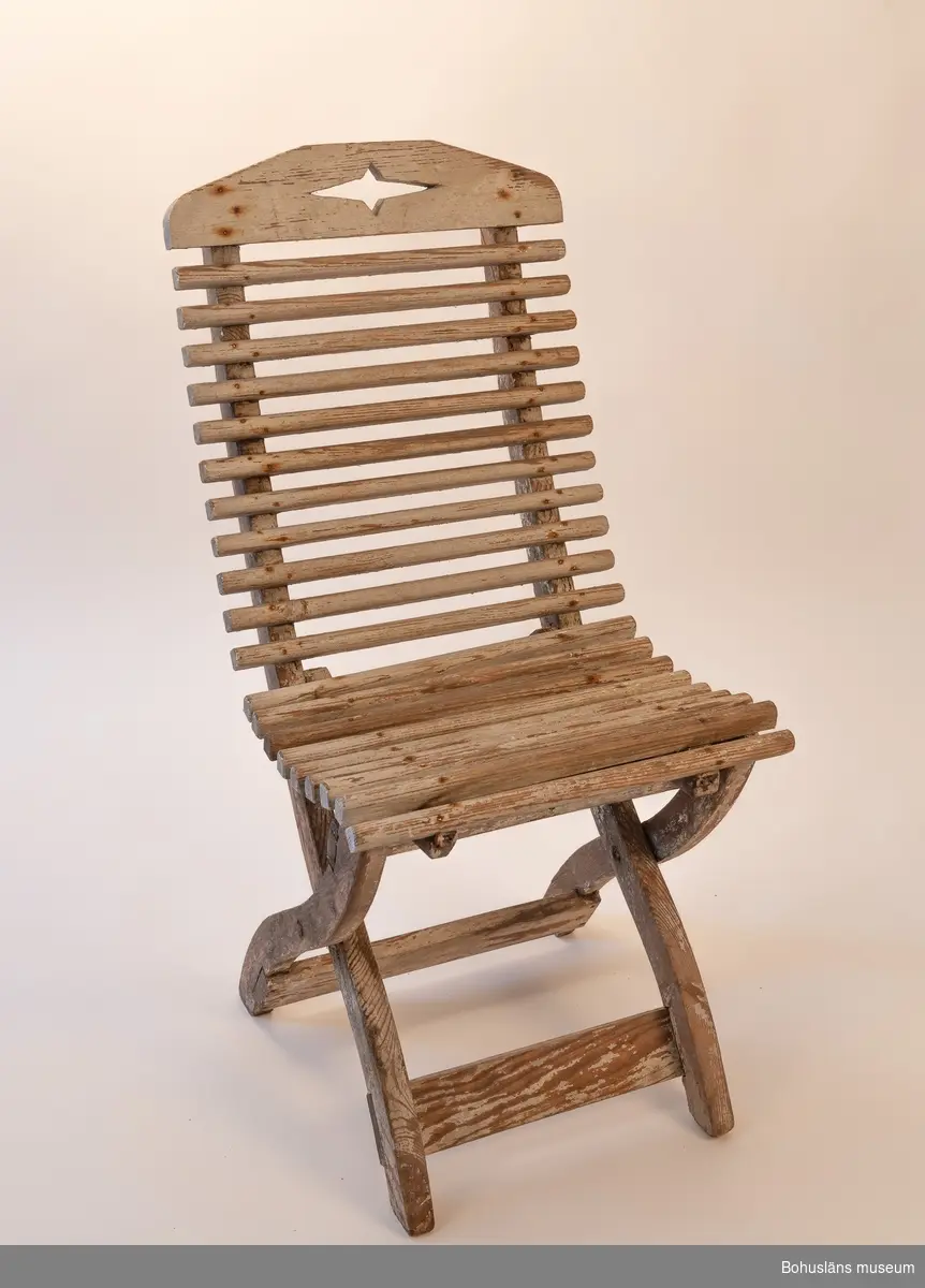 Vitmålad trästol, hopfällbar. Sits av rundade kraftiga spjälor. Dekorativt utformade benavslut och ryggbricka med utsågad stjärnform.
Samhör med UM032292 Bord.