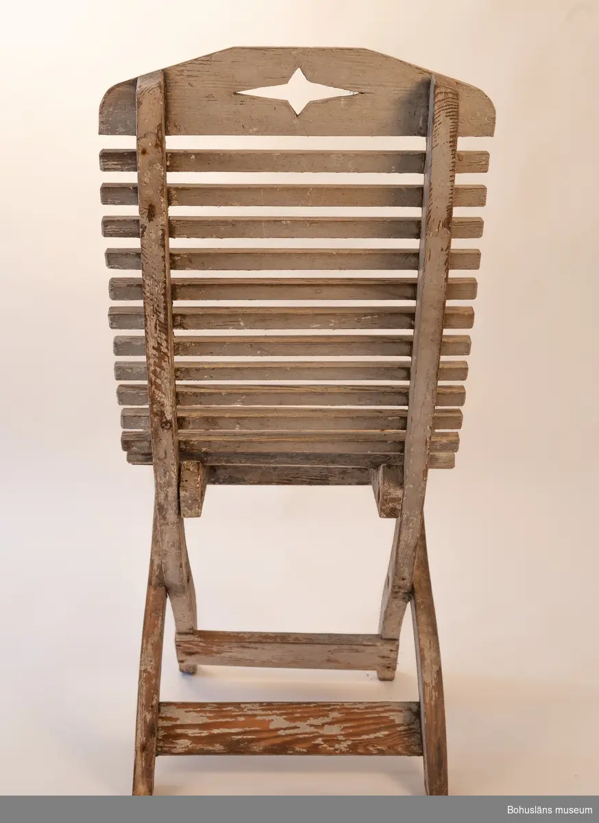 Vitmålad trästol, hopfällbar. Sits av rundade kraftiga spjälor. Dekorativt utformade benavslut och ryggbricka med utsågad stjärnform.
Samhör med UM032292 Bord.