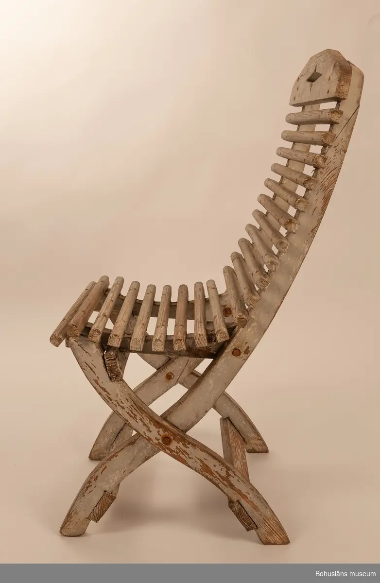Vitmålad trästol, hopfällbar. Sits av rundade kraftiga spjälor. Dekorativt utformade benavslut och ryggbricka med utsågad stjärnform.
Samhör med UM032292 Bord.