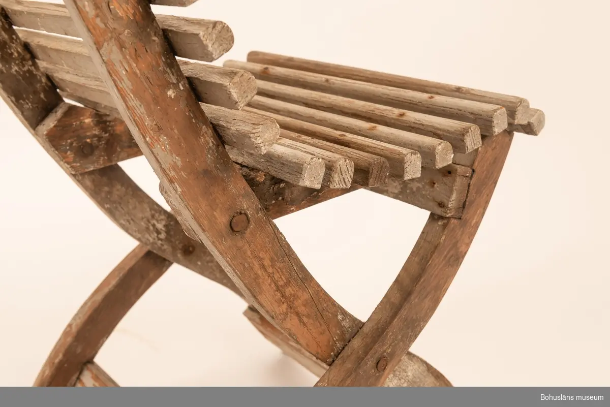 Vitmålad trästol, hopfällbar. Sits av rundade kraftiga spjälor. Dekorativt utformade benavslut och ryggbricka med utsågad stjärnform.
Samhör med UM032292 Bord.