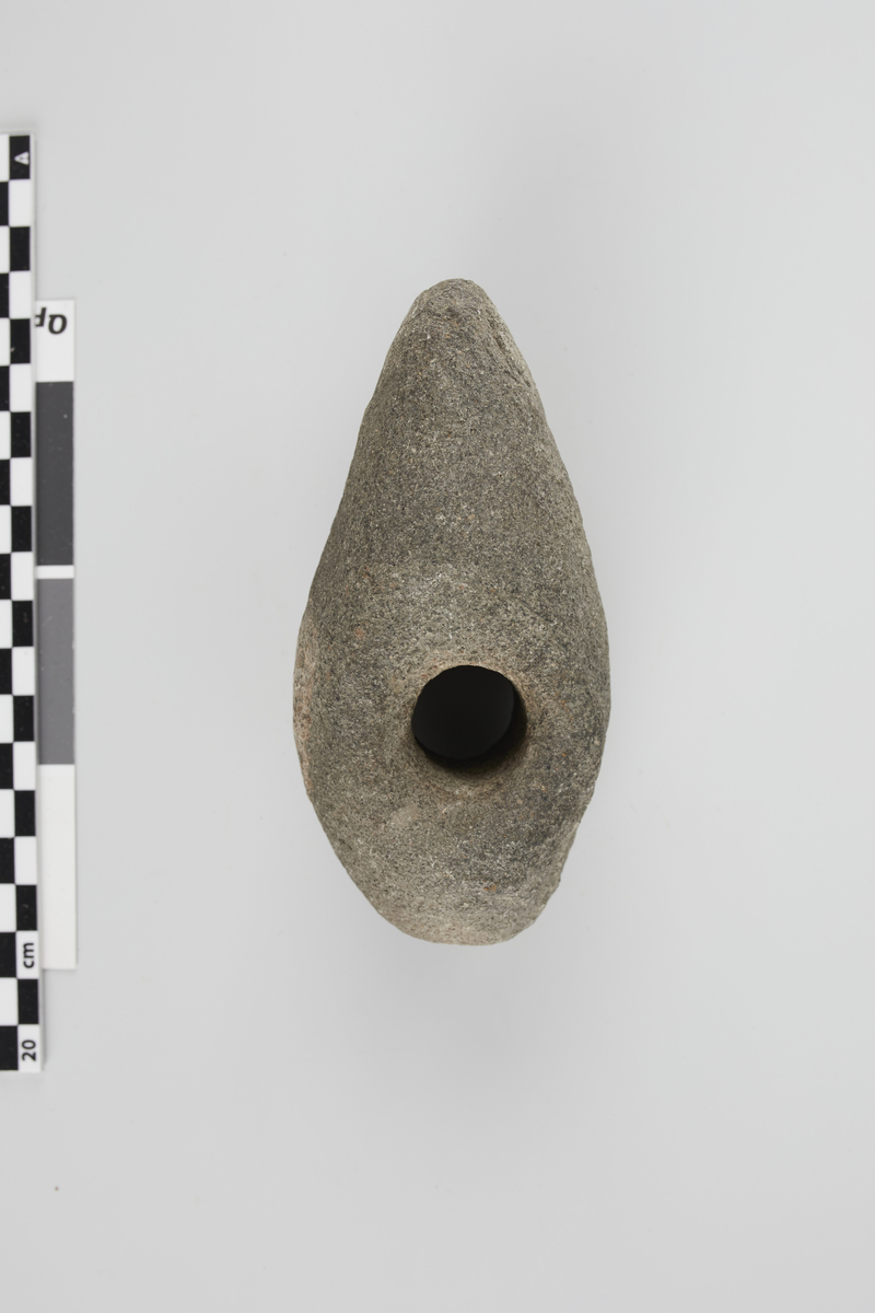 Stenøks med skafthul, stærkt forvitret; afrundet bane, eggen but, over- og underside svagt hvælvet, siderne rette, kanterne afrundede. 12,5 cm. lang, 6,1 cm. høi foran hullet, 6 cm. bred over hullet.