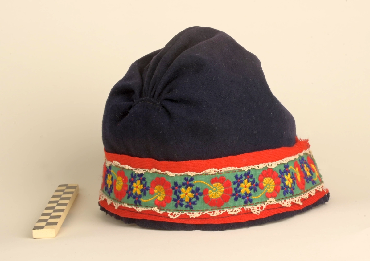 Kofte med lue, belte, forkle og sjal. Lua har dekorbånd nederst langs rimmen. Selve kofta har vevde dekorasjonsbånd på jakkeermene, kragen, oppe på og langs skuldrene, og nederst på kofta. Beltet til kofta låses ved lærreim som tres inn i lås med låsepinne - alt av stål. Selve låsen skjules av beltet da lærreim og lås er på baksiden av beltet. Beltets ende er avsluttet av tynt flettet bånd. Båndet festes i tinnknapp som er på utsiden av beltet. Dette er ei dekorativ løsning for å skjule den funksjonelle stållåsen. Forklet er blått, og dekorert med hvite snøkrystaller og blomster. Blomstene er gule, røde og blå blomser.  Kofta er i svart som er hovedfargen på kofta såvel som lua, mens dekorbånd og lue har andre farger.