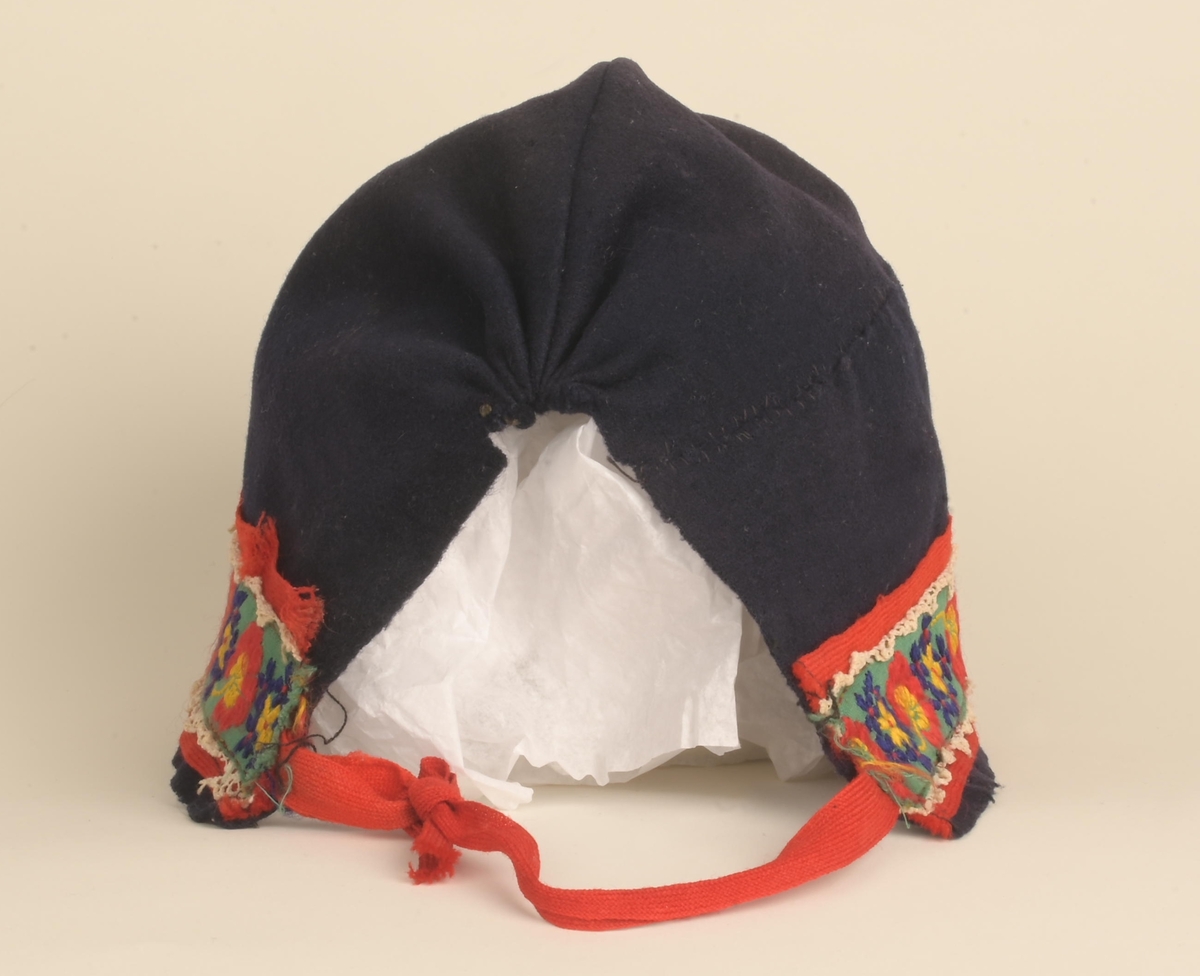 Kofte med lue, belte, forkle og sjal. Lua har dekorbånd nederst langs rimmen. Selve kofta har vevde dekorasjonsbånd på jakkeermene, kragen, oppe på og langs skuldrene, og nederst på kofta. Beltet til kofta låses ved lærreim som tres inn i lås med låsepinne - alt av stål. Selve låsen skjules av beltet da lærreim og lås er på baksiden av beltet. Beltets ende er avsluttet av tynt flettet bånd. Båndet festes i tinnknapp som er på utsiden av beltet. Dette er ei dekorativ løsning for å skjule den funksjonelle stållåsen. Forklet er blått, og dekorert med hvite snøkrystaller og blomster. Blomstene er gule, røde og blå blomser.  Kofta er i svart som er hovedfargen på kofta såvel som lua, mens dekorbånd og lue har andre farger.