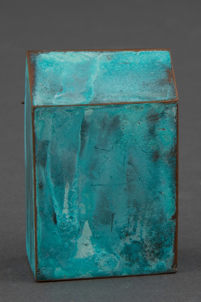 Brosje i patinert kobber. Brosjen har en arketypisk vertikal husform.