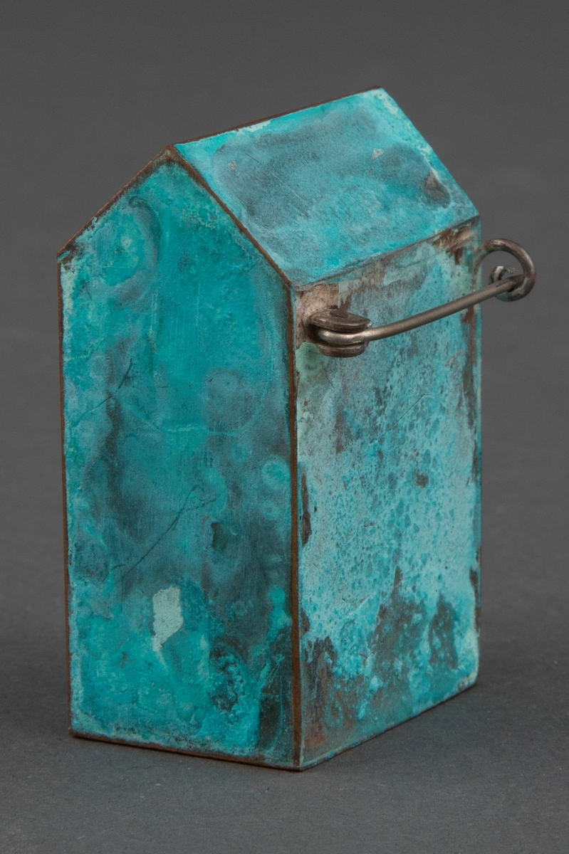 Brosje i patinert kobber. Brosjen har en arketypisk vertikal husform.