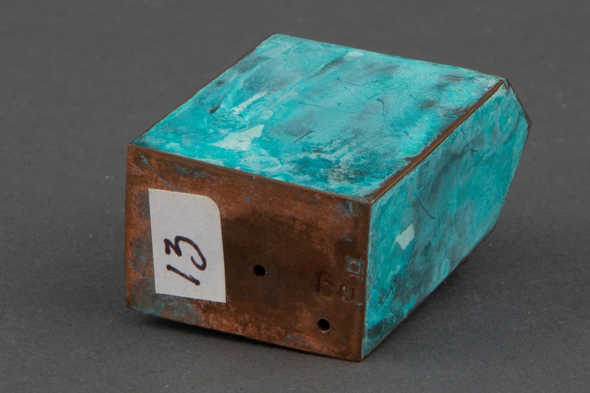 Brosje i patinert kobber. Brosjen har en arketypisk vertikal husform.